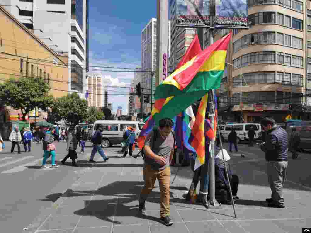 Un jóven camina en el centro de La Paz, Bolivia, mientras un vendedor exhibe la bandera nacional y las whipalas, que recientemente han tenido una mayor demanda.