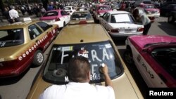 FILE - A local taxi driver paints "Uber out" on the back window of his car during a protest in Mexico City, May 25, 2015.