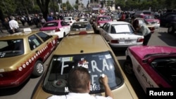 FILE - A local taxi driver paints "Uber out" on the back window of his car during a protest in Mexico City, May 25, 2015.