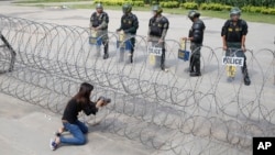 A Cambodian woman takes a photo of riot police standing behind bard wire at Freedom Park in Phnom Penh, Cambodia, May 1, 2014. 