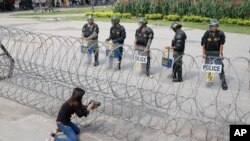 FILE - A Cambodian woman takes a photo of riot police standing behind bard wire at Freedom Park in Phnom Penh, May 1, 2014. U.S.-based Cambodian community activists are campaigning for a congressional resolution calling for human rights, democracy and the rule of law in Cambodia.