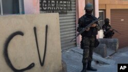 FILE - A soldier stands guard next to a wall tagged with the acronym "CV" identifying the criminal organization "Comando Vermelho" or Red Command, during an operation at the Rocinha slum, in Rio de Janeiro, Brazil, Tuesday, Oct. 10, 2017. 