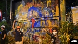 Pro-democracy protesters pose next to a paint-splattered sign for the police headquarters, during an anti-government rally in Bangkok, Thailand, Nov. 18, 2020. 