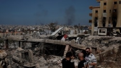 FILE: Orang-orang berdiri di bangunan-bangunan yang hancur akibat serangan udara Israel, di distrik Choueifat, Beirut, Lebanon, 3 Oktober 2024. (Louisa Gouliamaki/REUTERS)