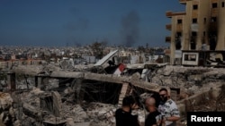 FILE: Orang-orang berdiri di bangunan-bangunan yang hancur akibat serangan udara Israel, di distrik Choueifat, Beirut, Lebanon, 3 Oktober 2024. (Louisa Gouliamaki/REUTERS)