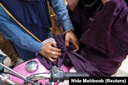 Humaira Rafaqat teaches a woman how to properly tie an abaya while riding a motorbike, during a motorbike training session, October 1, 2024. (REUTERS/Nida Mehboob)