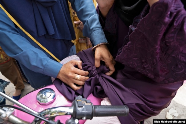 Humaira Rafaqat teaches a woman how to properly tie an abaya while riding a motorbike, during a motorbike training session, October 1, 2024. (REUTERS/Nida Mehboob)