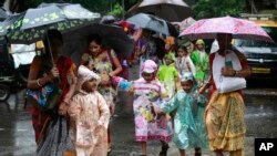 Mothers walk with their children wearing raincoats as they cross a flooded road in Mumbai, India, Tuesday, July 26, 2016.