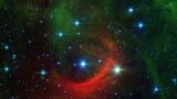 The red arc in this infrared image from NASA&#39;s Spitzer Space Telescope is a giant shock wave, created by a speeding star known as Kappa Cassiopeiae. It is a massive, hot supergiant moving at around 2.5 million mph relative to its neighbors (1,100 kilometers per second). But what really makes the star stand out is the surrounding, streaky red glow of material called a bow shock, in its path. (Image Credit: NASA/JPL-Caltech)