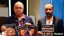 FILE —Avihai Brodutch, whose wife and three children were abducted, Gilad Korngold, whose son, daughter-in-law and two grandchildren were kidnapped by Hamas, pose for a photograph with pictures of their missing relatives, in Berlin, Germany, November 15, 2023.