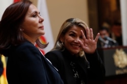 Accompanied by Bolivia's Foreign Minister Karen Longaric, interim President Jeanine Anez waves to journalists during a protocol greeting of ambassadors in Bolivia, Nov. 22, 2019.