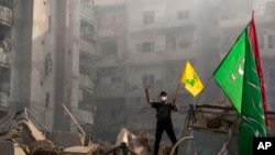 A man flashes the victory sign as holds up a Hezbollah flag while standing on the ruins of his destroyed apartment at the site of an Israeli airstrike in Dahiyeh, Beirut, Lebanon, Nov. 1, 2024. 