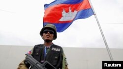 Seorang penjaga keamanan berdiri di bawah bendera Kamboja sambil membawa senjata, di ibu kota Phnom Penh, 16 November 2012. (REUTERS/Damir Sagolj)