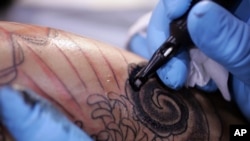 A tattoo artist applies ink to a customer's skin.