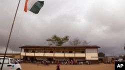 FILE - An Ivory Coast national flag, left, is seen at a polling station as people line up to vote in Abidjan, Ivory Coast, Oct. 25, 2015. Last year's orderly presidential election in the country was cited among the reasons for the lifting of sanctions.