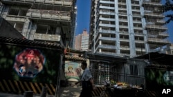 FILE - A man walks by a fruits vendor waiting for customers outside a luxury housing construction site in Beijing, Sept. 24, 2024. 