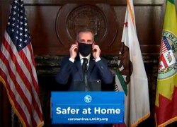 This still image taken from a live stream provided by Office of Mayor Eric Garcetti showing Los Angeles Mayor Garcetti displaying putting on a protective face mask during his daily news conference in Los Angeles, April 1, 2020.