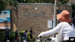 A security guard stands on duty as residents pass by the Canadian Embassy in Beijing on Friday, June 19, 2020. Chinese prosecutors charged two detained Canadians with spying Friday in an apparent bid to step up pressure on Canada to drop a U.S…