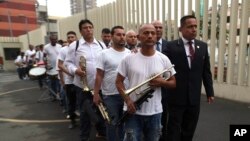 In this July 19, 2019 photo, accompanied by prison guards, inmates stand in a line holding their instruments, after arriving at the national theater in Lima, Peru, to take part in a music session with the symphony orchestra. (AP Photo/Martin Mejia)