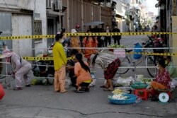 Personas compran verduras junto a una barricada instalada en un vecindario debido a un cierre ordenado por las autoridades estatales para tratar de detener un aumento en los casos del coronavirus Covid-19 en Phnom Penh el 25 de abril de 2021.