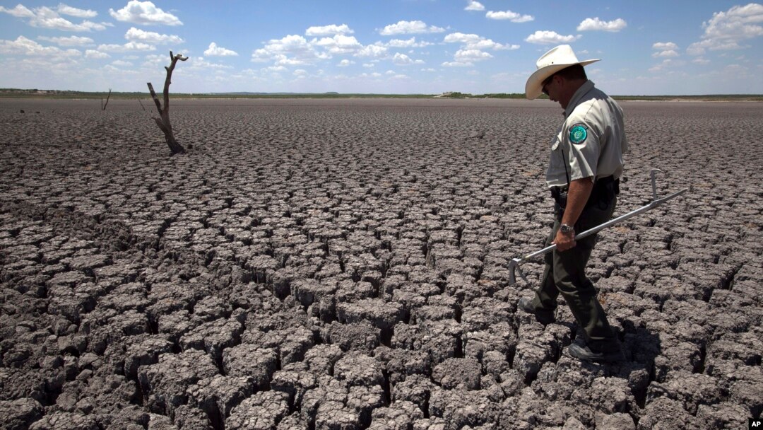 FILE - A Texas State Park police officer walks across a cracked lake bed in San Angelo, Texas, Aug. 3, 2011.