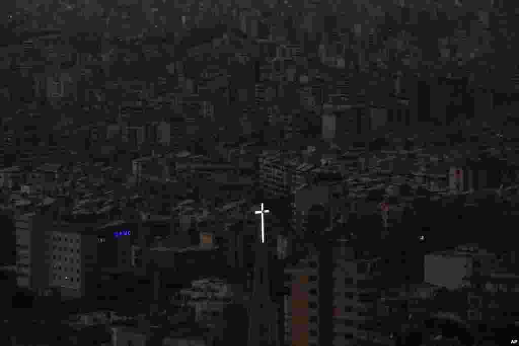 The cross atop of Our Lady of Hadath Church appears in front Dahiyeh suburb, background, that remains in darkness after Israeli airstrikes, Lebanon.