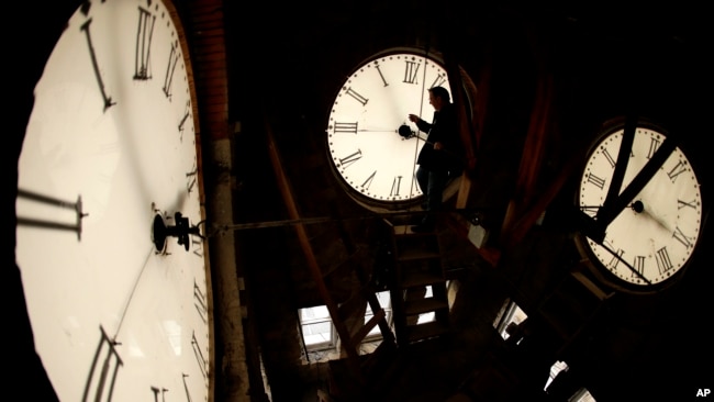 FILE - Custodian Ray Keen inspects a clock face before changing the time on the 100-year-old clock atop the Clay County Courthouse, March 8, 2014, in Clay Center, Kansas. (AP Photo/Charlie Riedel, File)
