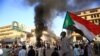 FILE - A Sudanese man wearing a face mask waves his country's national flag during protests in Khartoum to mark the second anniversary of the start of a revolt that toppled the previous government, Dec. 19, 2020.