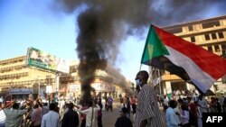 FILE - A Sudanese man wearing a face mask waves his country's national flag during protests in Khartoum to mark the second anniversary of the start of a revolt that toppled the previous government, Dec. 19, 2020.