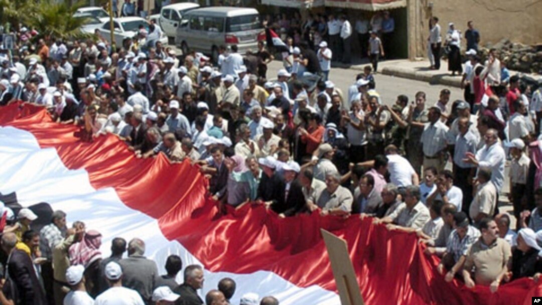Syrian supporters of President Bashar Assad carry a giant national flag during a protest in al-Qarya village, in the southwestern Suwayda province, Syria, July 1, 2011