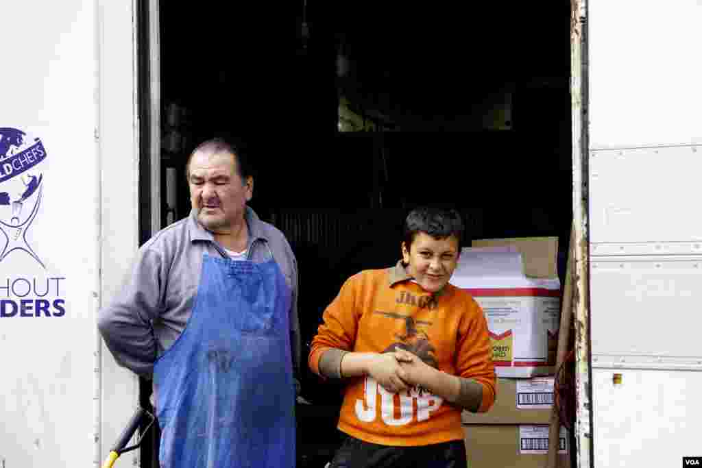 Seorang ayah dan anak asal Yunani menunggu pembagian makanan untuk para pengungsi Idomeni. (VOA/Jamie Dettmer)