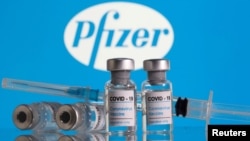 FILE - Vials labelled 'COVID-19 Coronavirus Vaccine' and a syringe are seen in front of the Pfizer logo in this illustration taken Feb. 9, 2021.