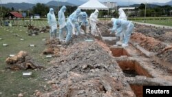 Trabajadores con trajes protectores entierran a una víctima del COVID-19 en un cementerio, en las cuevas de Batu, Malasia, el 27 de enero de 2021.