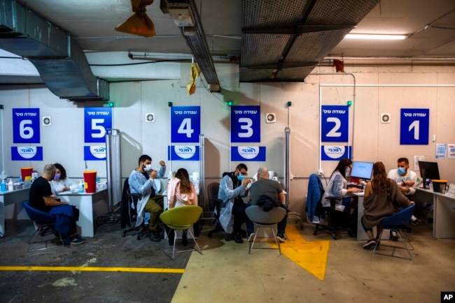 FILE - Israelis receive a Pfizer-BioNTech COVID-19 vaccine from medical professionals at a coronavirus vaccination center set up on a shopping mall parking lot in Givataim, Israel, Feb. 4, 2021.