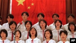 Murid-murid Sekolah Anak Pekerja Mongkok yang pro-China di Hong Kong, bernyanyi di depan bendera nasional China, 1 Oktober 1996. (AP/Vincent Yu). Mulai awal tahun depan, sekolah TK hingga SMA di Hong Kong wajib upacara bendera dan menyanyikan lagu kebangsaan seminggu sekali.