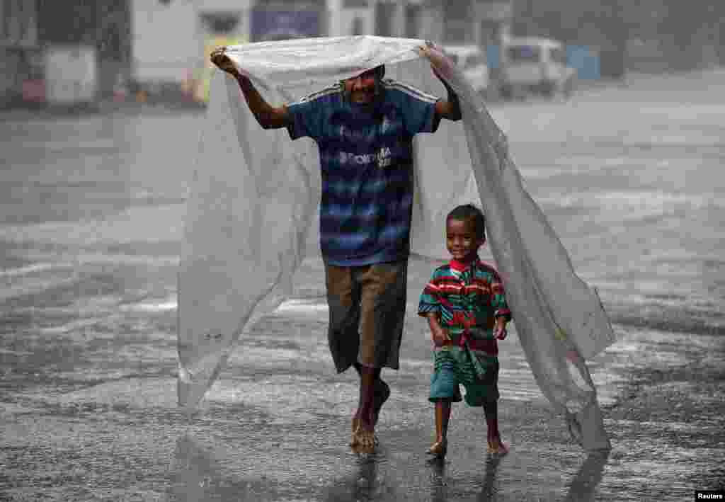 A homeless man and his son cover themselves with a plastic sheet to protect themselves from rain as they walk to a shelter in Kolkata, India.
