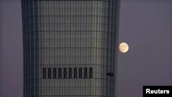 FILE - A moon is seen behind the construction site of China Zun in Beijing's central business area, Nov. 21, 2018. 