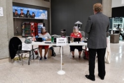 Poll workers wearing face shields assist a voter as he checks in to cast his vote in the Kentucky primary at the Kentucky Exposition Center in Louisville, Ky., June 23, 2020.