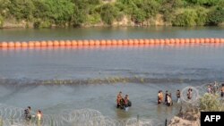 TOPSHOT - Migrants walk by a string of buoys placed on the water along the Rio Grande border with Mexico in Eagle Pass, Texas, on July 16, 2023.