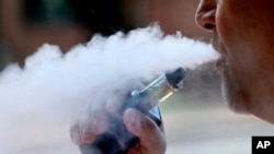 FILE - A man exhales while smoking an e-cigarette in Portland, Maine, Aug. 28, 2019. 