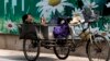 A migrant worker listens to radio on his tricycle cart parked next to a billboard promoting environment protection with the slogan "Environment protection starts from you and me" on display at the Central Business District of Beijing, June 5, 2017. 