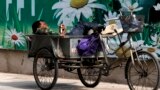 A migrant worker listens to radio on his tricycle cart parked next to a billboard promoting environment protection with the slogan "Environment protection starts from you and me" on display at the Central Business District of Beijing, June 5, 2017. 