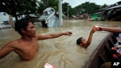 A boy receives food as a man waits near half-submerged residences in Nyaung Tone, in the Irrawaddy Delta, southwest of Yangon, Myanmar, Aug. 7, 2015. Dozens have died from recent weeks of flooding and more than hundreds of thousands have been affected.