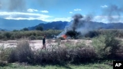 A man stands near the smoking remains of a helicopter that crashed with another near Villa Castelli in the La Rioja province of Argentina, March 9, 2015.