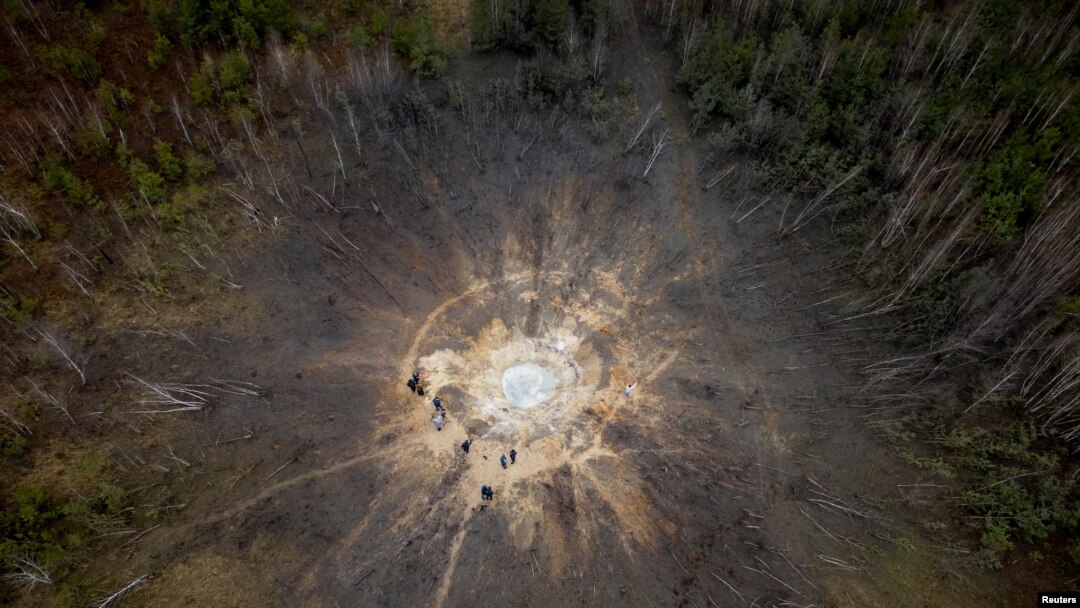 Orang-orang berdiri di sekitar kawah yang terbentuk akibat serangan rudal Rusia, di tengah serangan Rusia ke Ukraina, di desa Buda-Babynetska, di luar Bucha, dekat Kyiv, Ukraina 15 Februari 2024. (REUTERS/Thomas Peter)