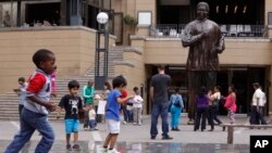 Children play beneath a giant statue of former South African President Nelson Mandela, center back, on Nelson Mandela Square in Sandton, Johannesburg, Sunday, Mar. 10, 2013.