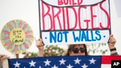 FILE - Lauren Rees holds up a sign during a rally against a scheduled visit by President Donald Trump, March 13, 2018, in San Diego.