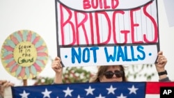 Una manifestante muestra un rótulo que pide "Construir puentes no muros", durante una protesta contra la visita del presidente Donald Trump en San Diego, California.