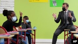 FILE - French President Emmanuel Macron talks with students during a visit in a school in Melun, south of Paris, April 26, 2021. The country's Ministry of Education this week took steps to make French more inclusive by feminizing some words.