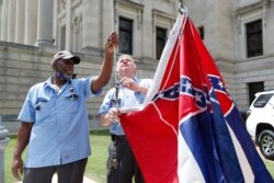 Mississippi Department of Finance and Administration employees Willie Townsend, left, and Joe Brown, attach Mississippi state flags to a harness before raising them over the Capitol grounds in Jackson, Mississippi, June 30, 2020.
